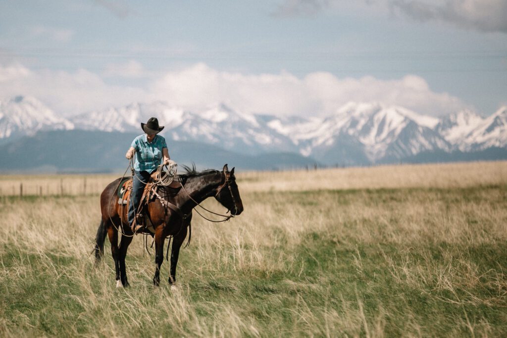 Hey cowgirl on her horse, gathering her rope at a branding with the beautiful mountains in the background